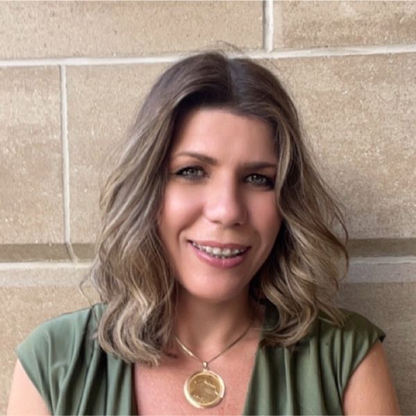 Image of Eleni standing in front of a beige wall and smiling.